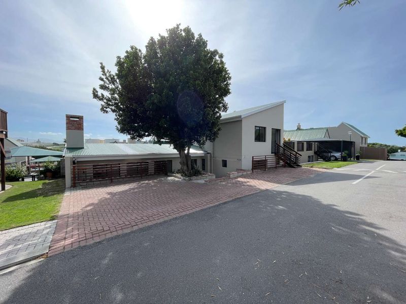 Front exterior view of the property featuring a brick paved driveway, metal railings, and a prominent tree, showcasing the building's facade and roof structure.