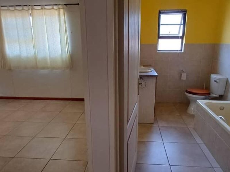 A view from a hallway looking into an empty bedroom and an adjacent bathroom featuring a built-in bathtub and vanity.