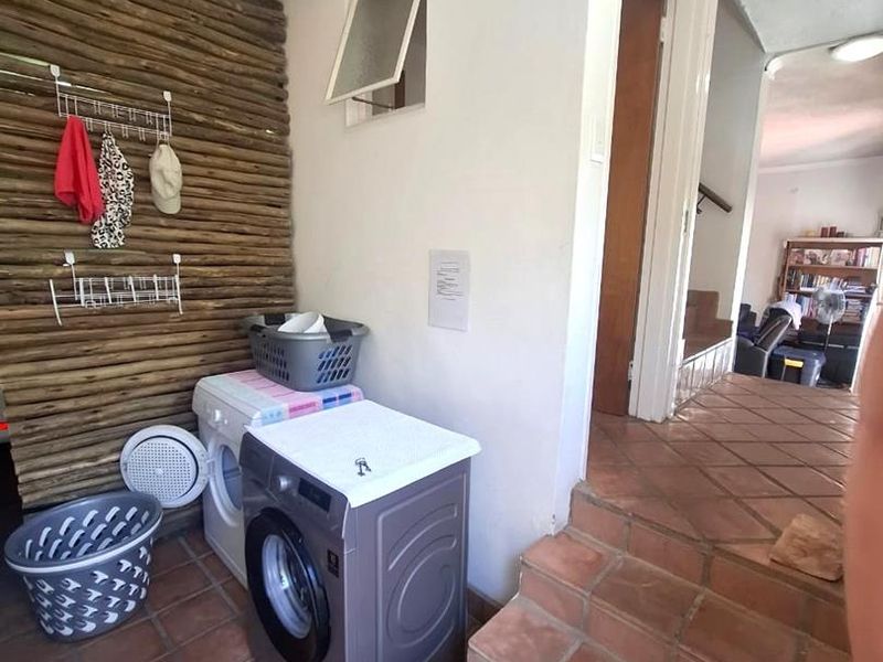 A functional laundry area featuring terracotta floor tiles, timber wall cladding, and direct access to the interior living space via a small staircase.