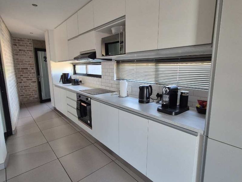 Modern galley-style kitchen featuring sleek white cabinetry, integrated appliances including an oven and microwave, subway tile backsplash, and large format floor tiles.