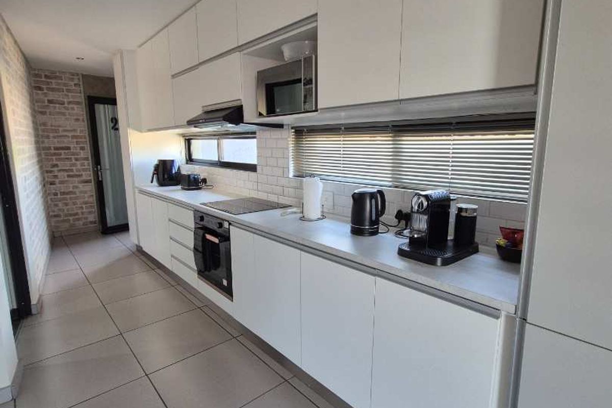 Modern galley-style kitchen featuring sleek white cabinetry, integrated appliances including an oven and microwave, subway tile backsplash, and large format floor tiles.