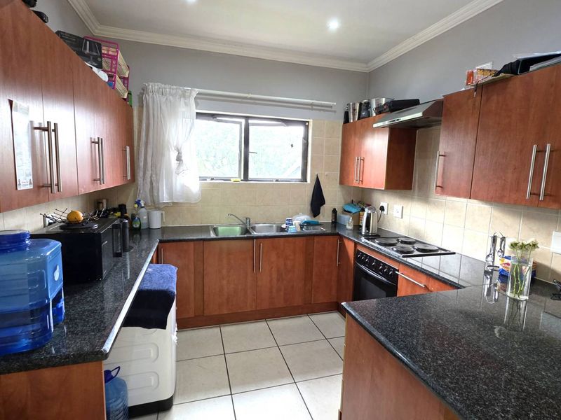 A functional kitchen featuring granite countertops, wooden cabinetry, built-in oven with hob, and tiled finishes throughout.