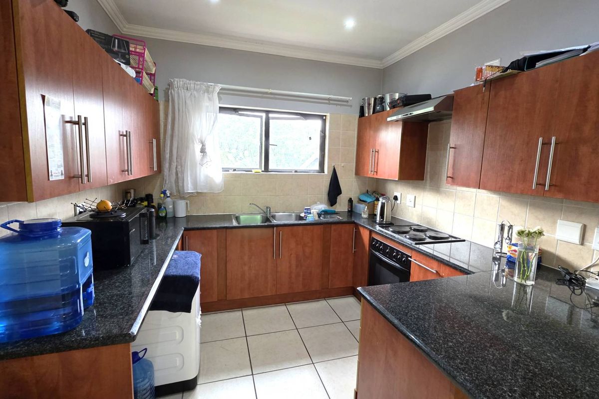A functional kitchen featuring granite countertops, wooden cabinetry, built-in oven with hob, and tiled finishes throughout.