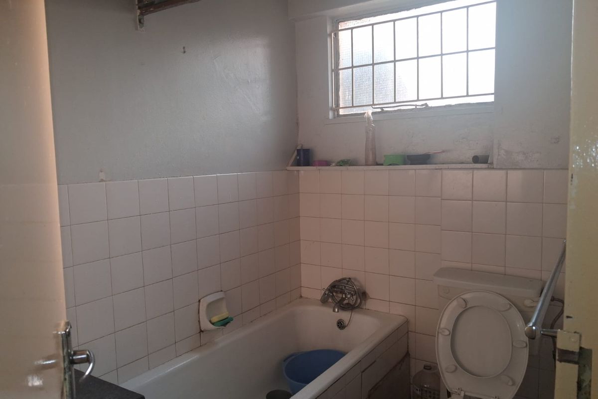 A functional bathroom featuring a bathtub, toilet, and tiled walls, requiring cosmetic updates to modernize the space.