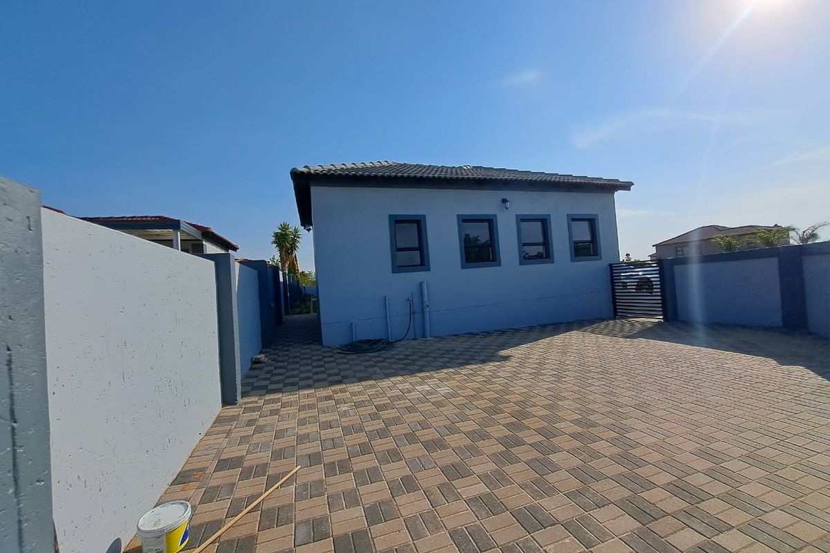 A view of the property's exterior rear area, featuring paved driveway space, perimeter boundary walls, and a tiled roof structure.