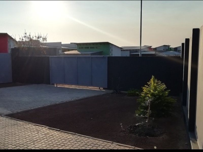 A view of the property entrance featuring a paved driveway, perimeter wall, and a sliding gate.