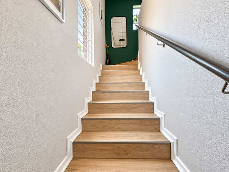 A well-maintained staircase featuring wood-look treads, white skirting boards, and a modern handrail, leading to an upper landing with a green accent wall.