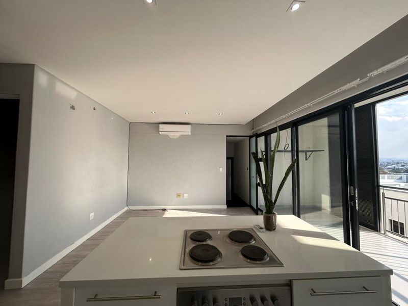 Open-plan living area featuring a kitchen island with built-in hob and oven, recessed lighting, and large sliding doors leading to a balcony.