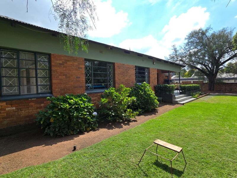 Rear view of a brick house featuring metal security window grilles, a corrugated metal roof, and a well-maintained garden with a lawn.