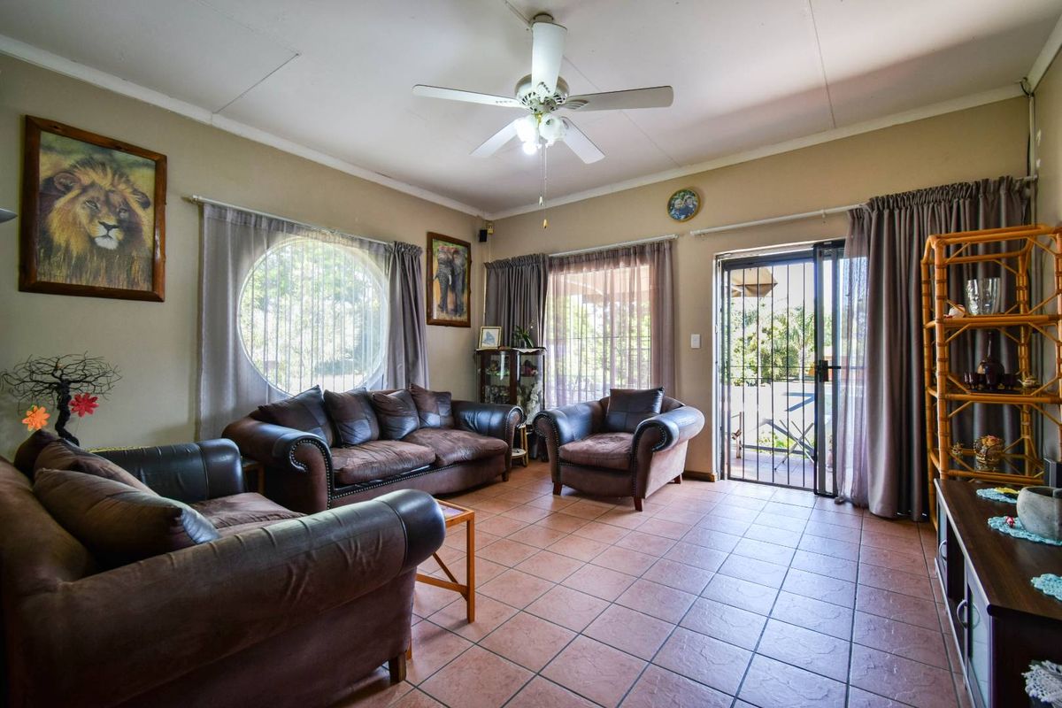 A spacious living room featuring ceramic tile flooring, a ceiling fan, a unique circular window, and direct access to the outdoor patio area.