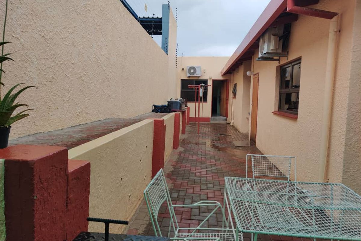 A paved side courtyard area featuring a low boundary wall, exterior lighting, and wall-mounted air conditioning units.