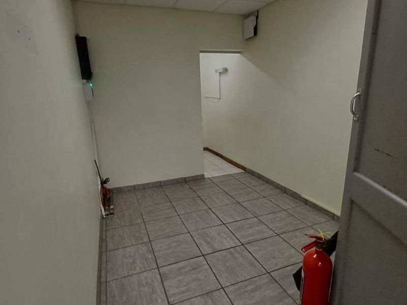 A functional, empty office space featuring tiled flooring, a suspended ceiling with integrated lighting, and a fire extinguisher.