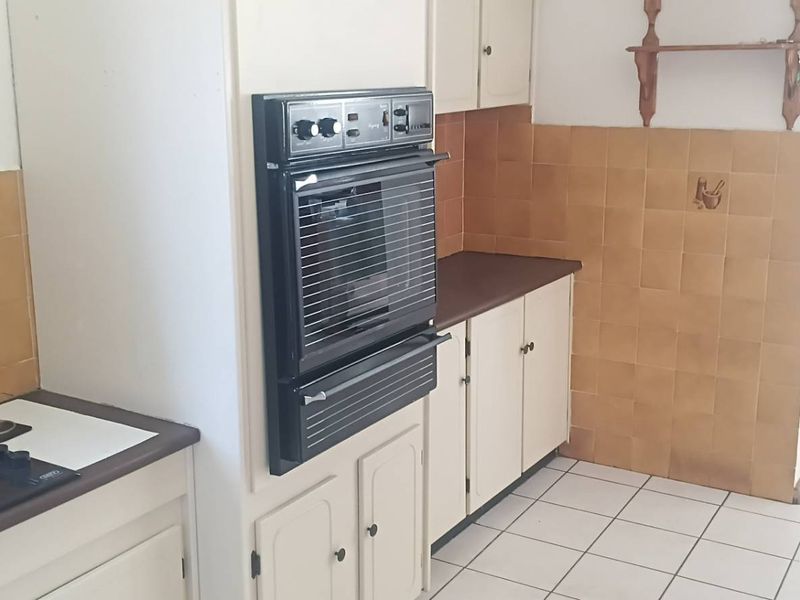 A functional kitchen featuring built-in cabinetry, a wall-mounted oven, electric hob, and tiled splashbacks, offering a blank canvas for modern renovation.