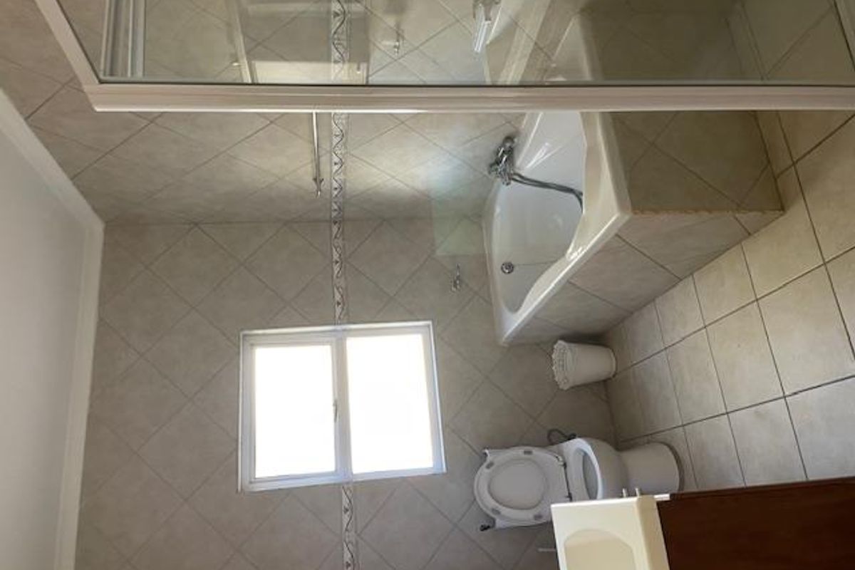A functional bathroom featuring a built-in bathtub, a toilet, and a vanity unit with tiled walls and flooring.