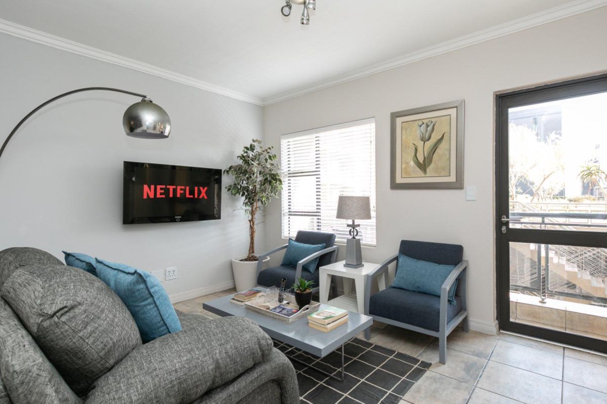 A bright and comfortable living room featuring tiled flooring, crown molding, and a glass-paneled door leading to an outdoor area.