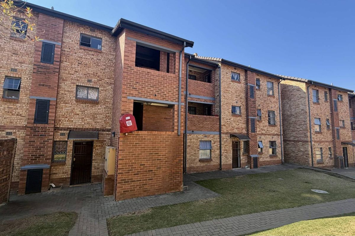 Exterior view of a multi-story apartment complex featuring face brick construction, paved walkways, and multiple balcony access points.