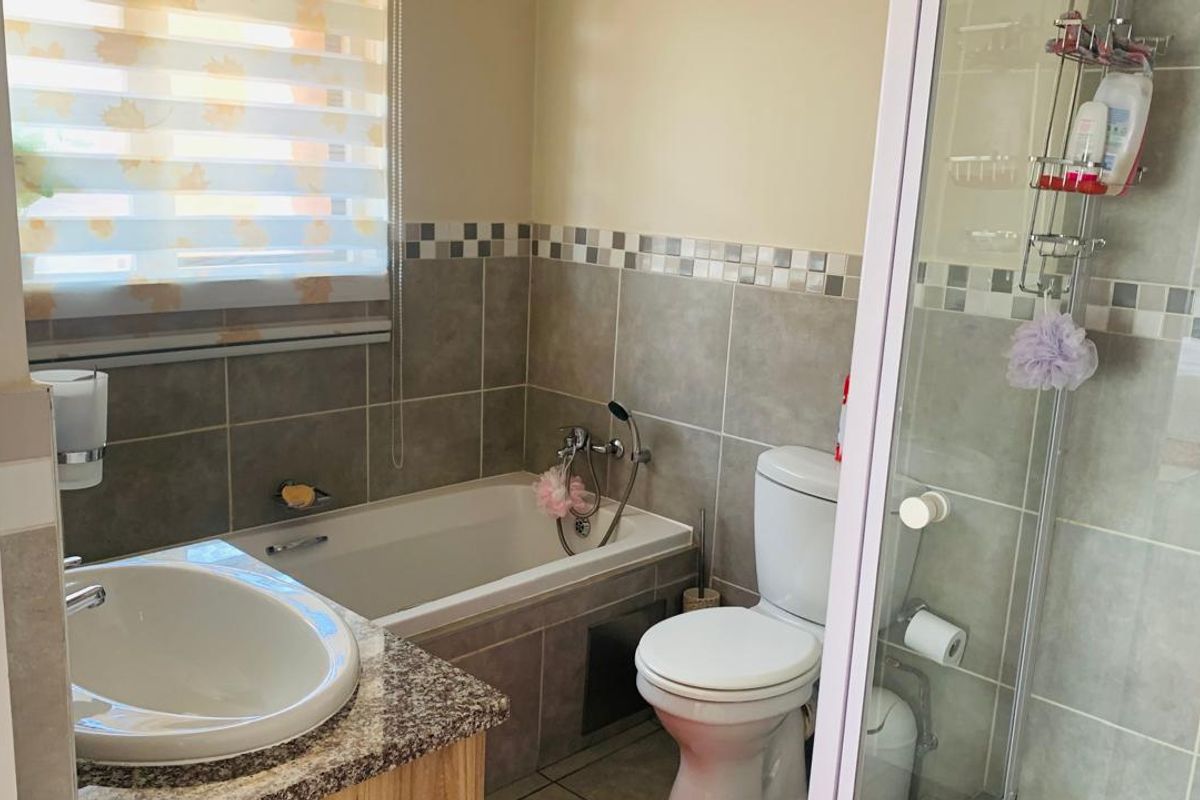 A functional bathroom featuring a built-in bathtub, a separate glass-enclosed shower, a vanity basin with a granite countertop, and a toilet.