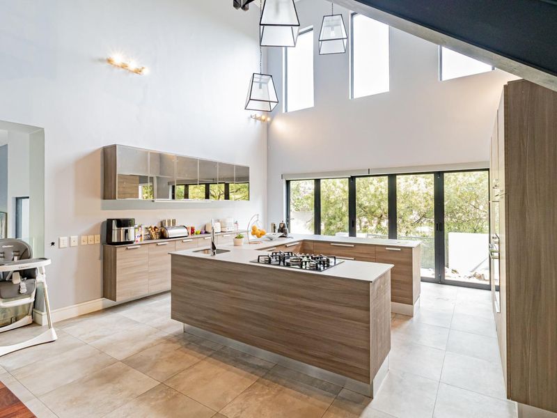 Modern open-plan kitchen featuring a central island with gas hob, sleek cabinetry, tiled floors, and high ceilings with abundant natural light.