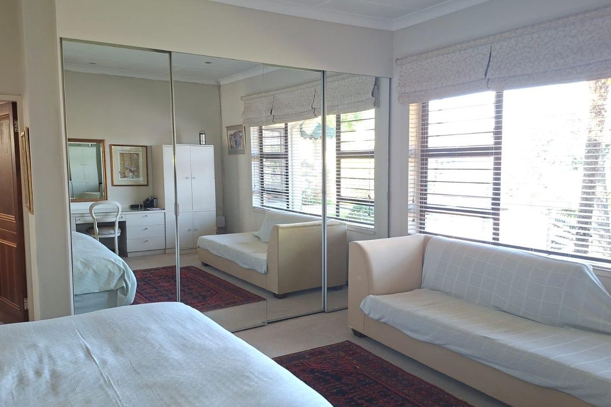 Spacious bedroom featuring large windows with blinds and extensive floor-to-ceiling mirrored sliding wardrobe doors, providing ample storage and natural light.