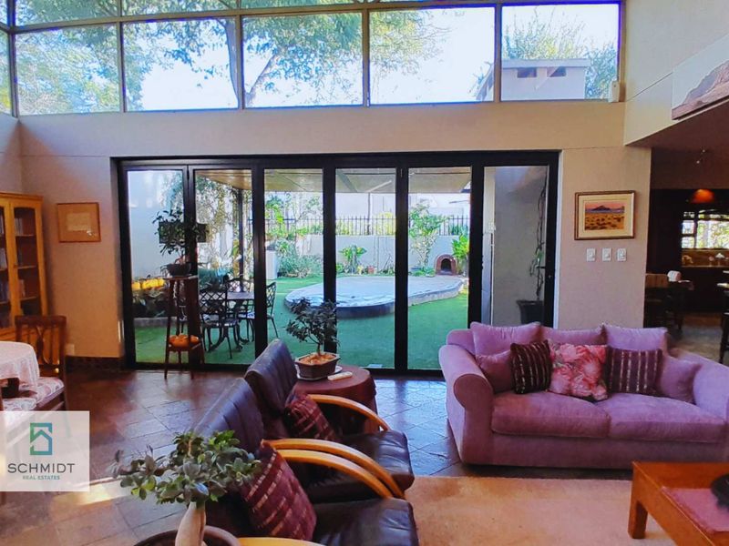 Spacious open-plan living area featuring high ceilings with clerestory windows, tiled flooring, and large bi-fold doors opening onto a private garden and patio.