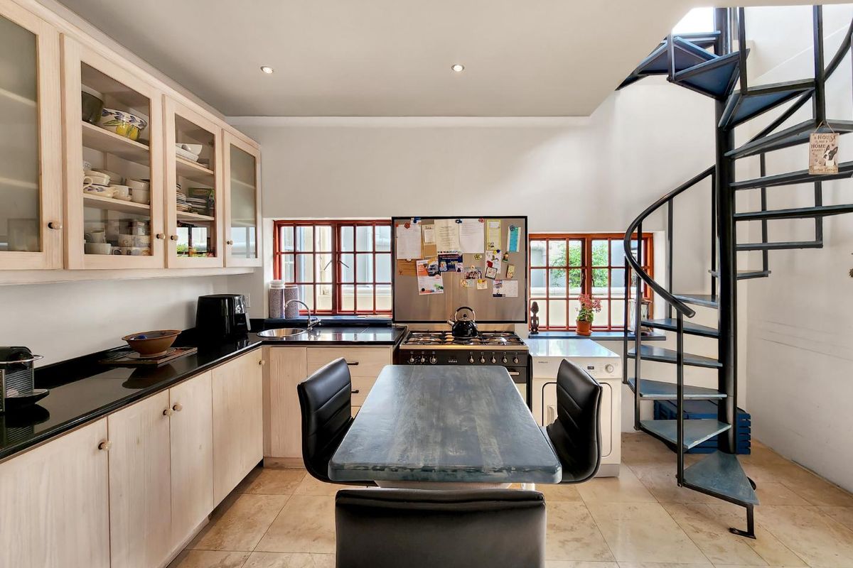 A functional kitchen featuring light wood cabinetry, black granite countertops, a gas stove, and a distinctive spiral staircase leading to the upper level.