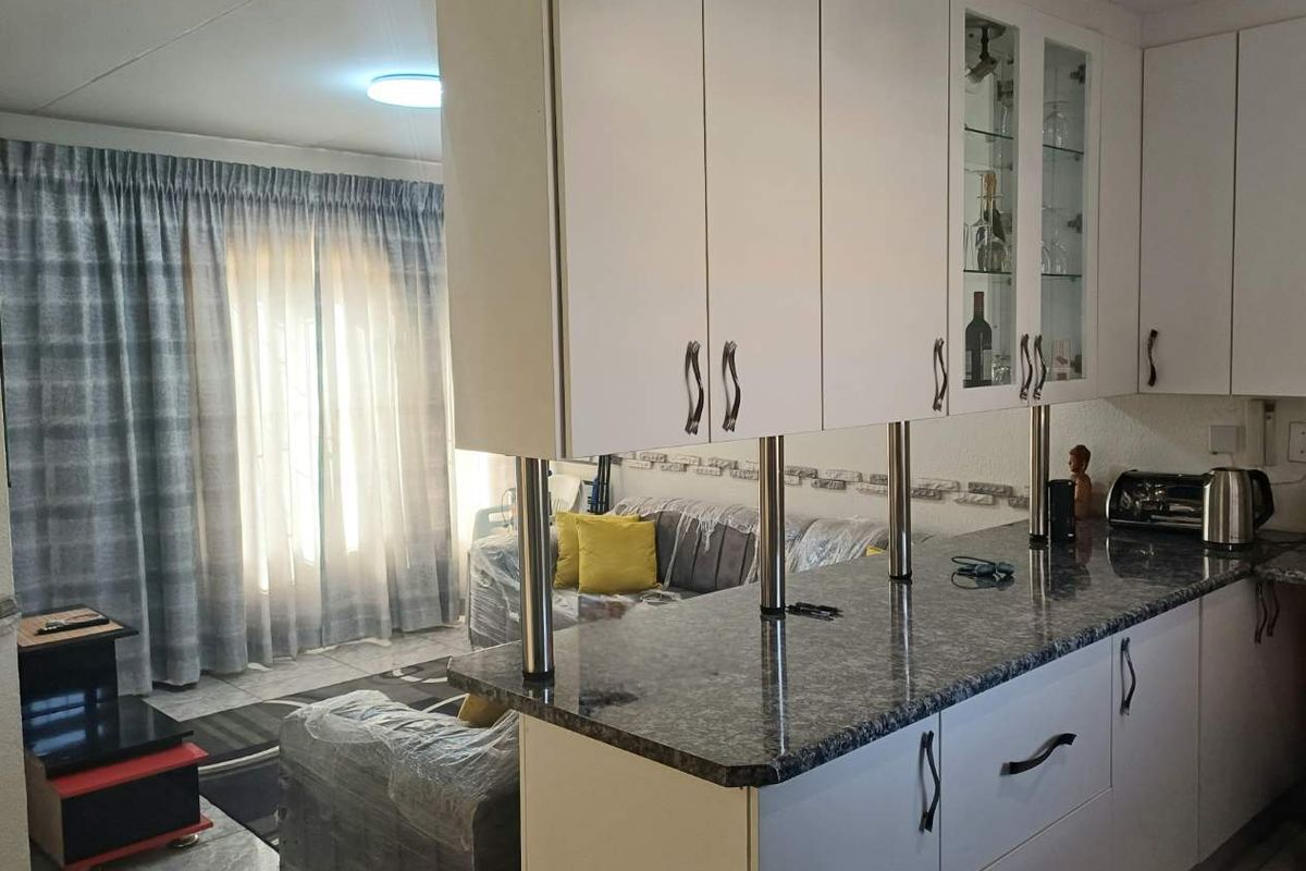 Open-plan kitchen and living area featuring white cabinetry, granite countertops, a breakfast bar, and tiled flooring throughout.