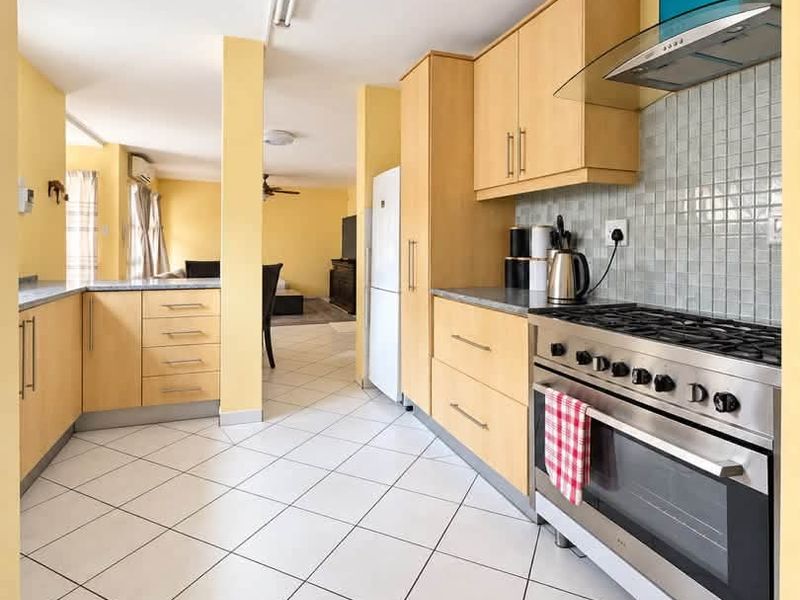 Open plan kitchen featuring light wood cabinetry, tiled flooring, and a stainless steel gas stove with an extractor fan, flowing into the living area.