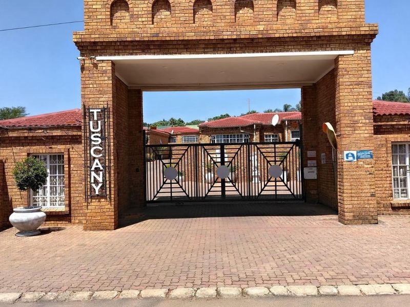 The front entrance of the Tuscany complex features a prominent brick archway, secure gated access, and a well-maintained paved driveway.