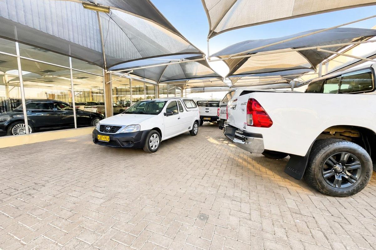 A commercial retail exterior featuring a paved parking area covered by shade cloth canopies and large glass storefront windows.
