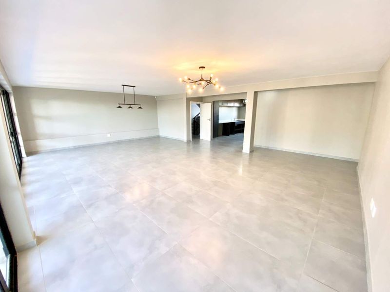 Spacious open-plan living area featuring large format floor tiles, modern lighting fixtures, and seamless access to outdoor space through sliding glass doors.