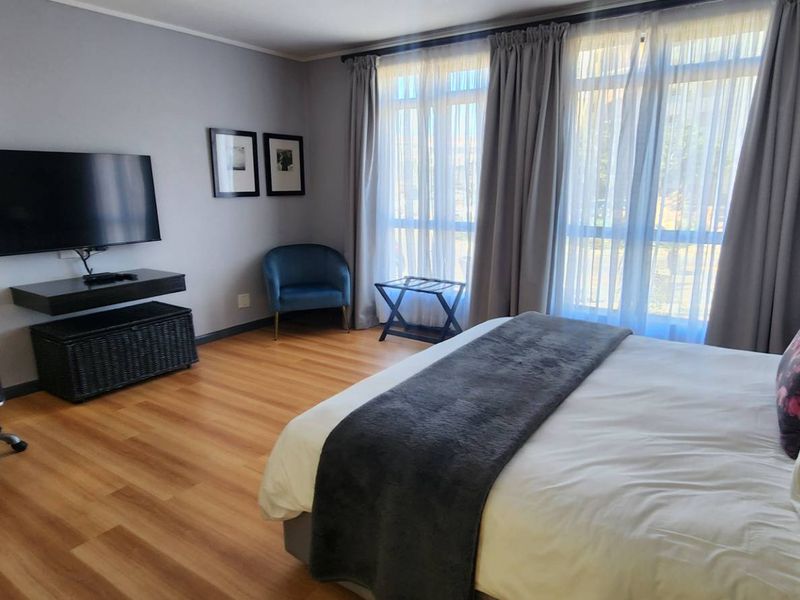 A well-maintained bedroom featuring laminate flooring and large windows with curtains, providing a comfortable and functional living space.