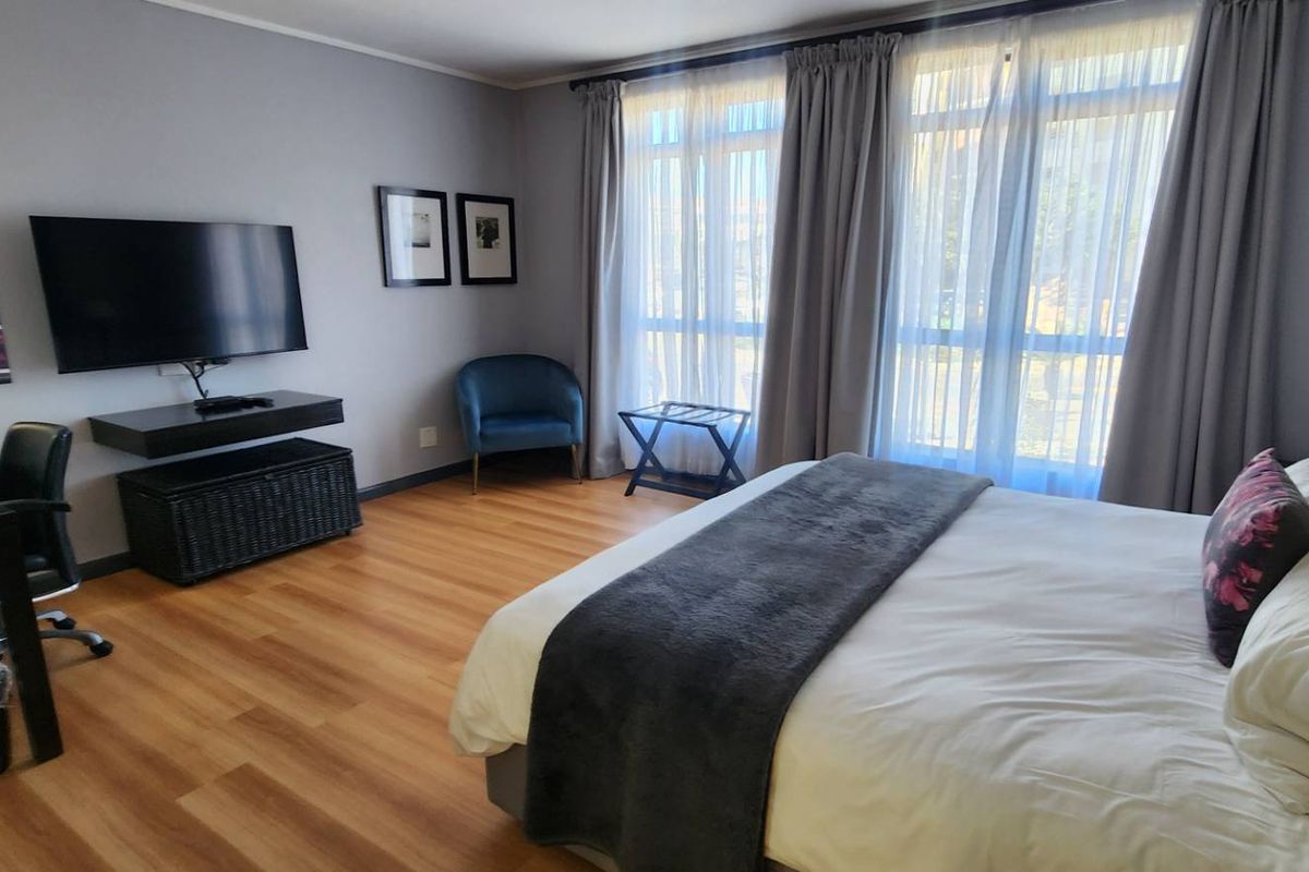 A well-maintained bedroom featuring laminate flooring and large windows with curtains, providing a comfortable and functional living space.