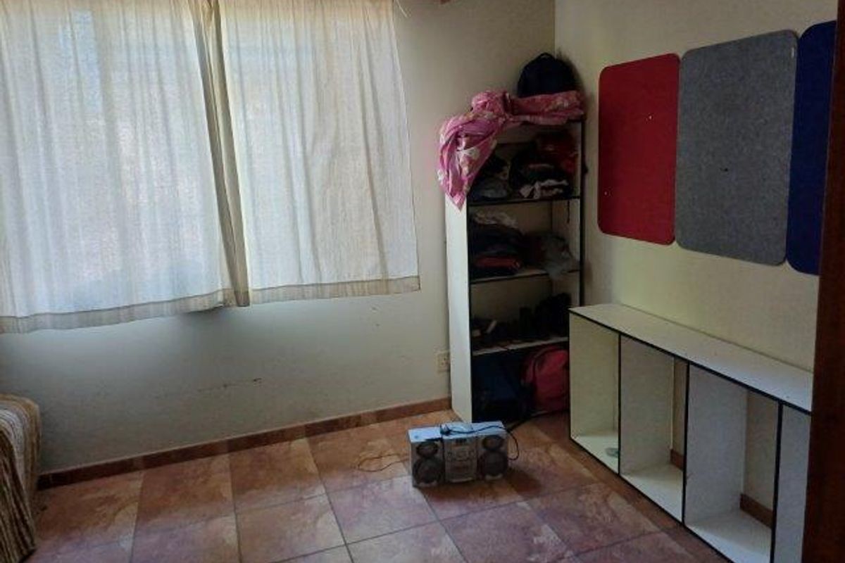 A bedroom featuring tiled flooring, a large window with curtains, and built-in wall-mounted display shelving.