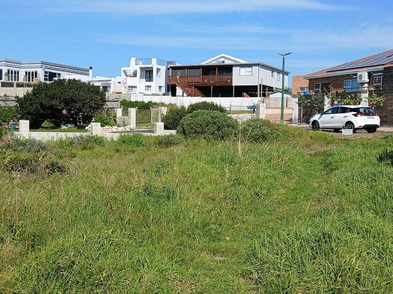 A vacant residential plot featuring natural grass coverage, boundary walling, and established neighborhood surroundings.