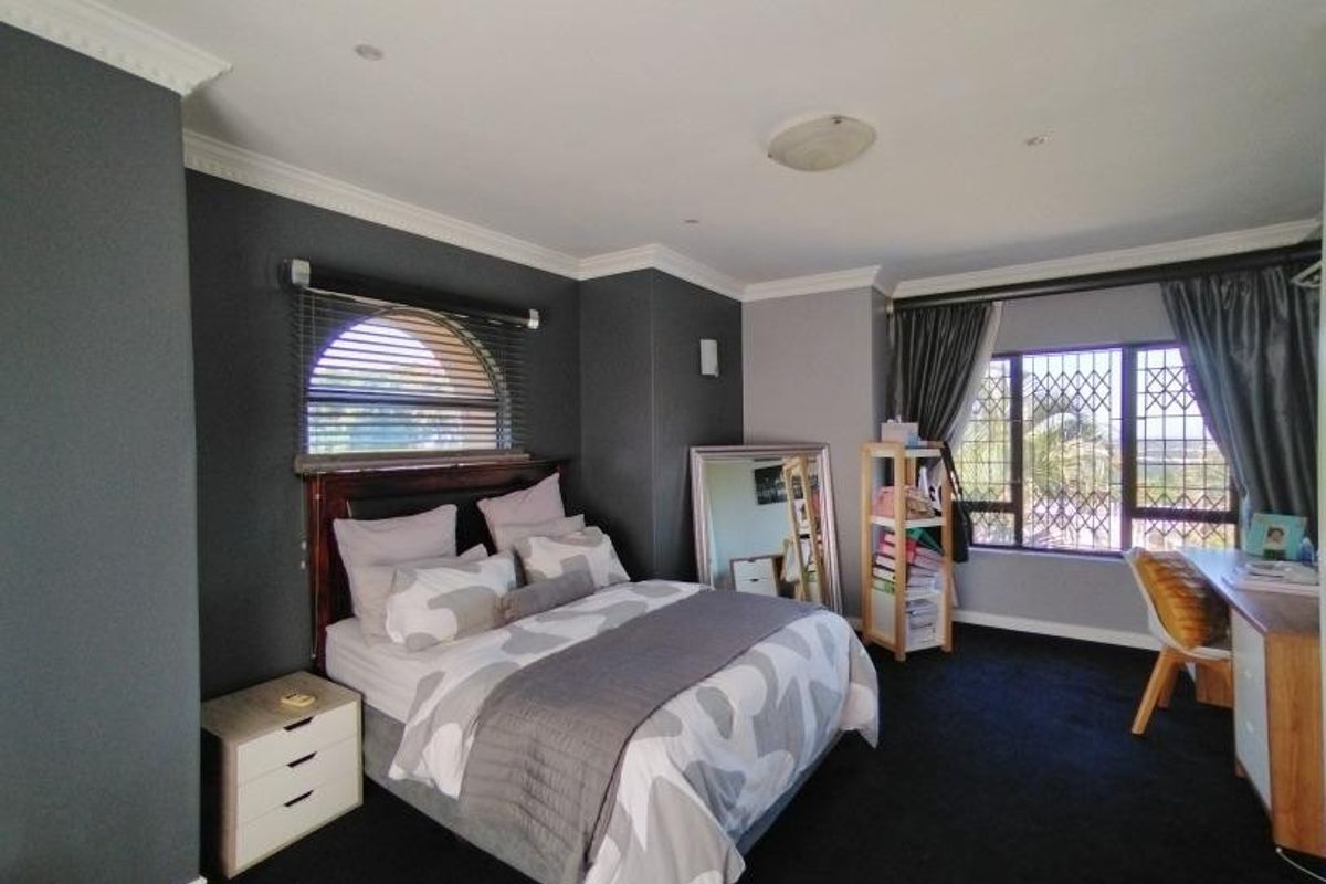 Spacious bedroom featuring dark accent walls, crown molding, recessed lighting, and large windows with security bars.