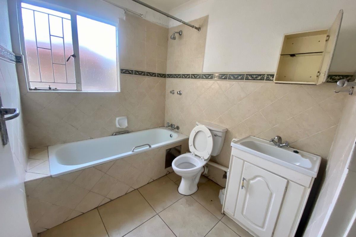 A dated bathroom featuring a built-in bathtub, toilet, and vanity cabinet with tiled walls and flooring.