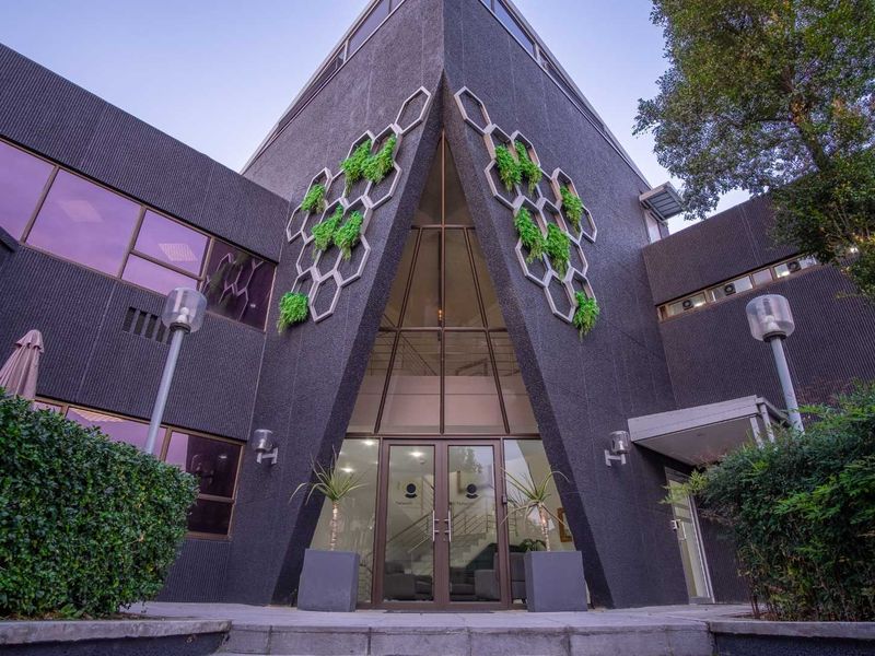 Modern office building entrance featuring a striking angular glass facade, dark textured cladding, and decorative honeycomb architectural elements.