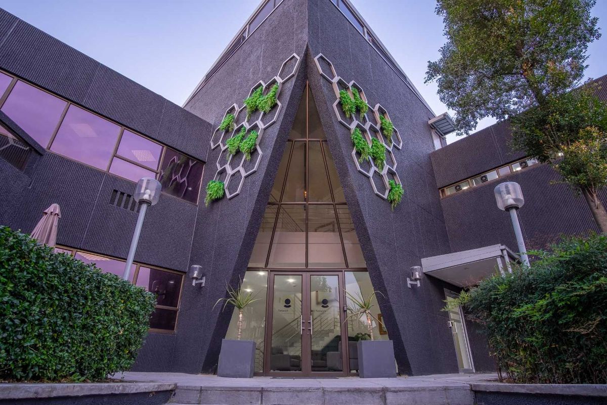 Modern office building entrance featuring a striking angular glass facade, dark textured cladding, and decorative honeycomb architectural elements.