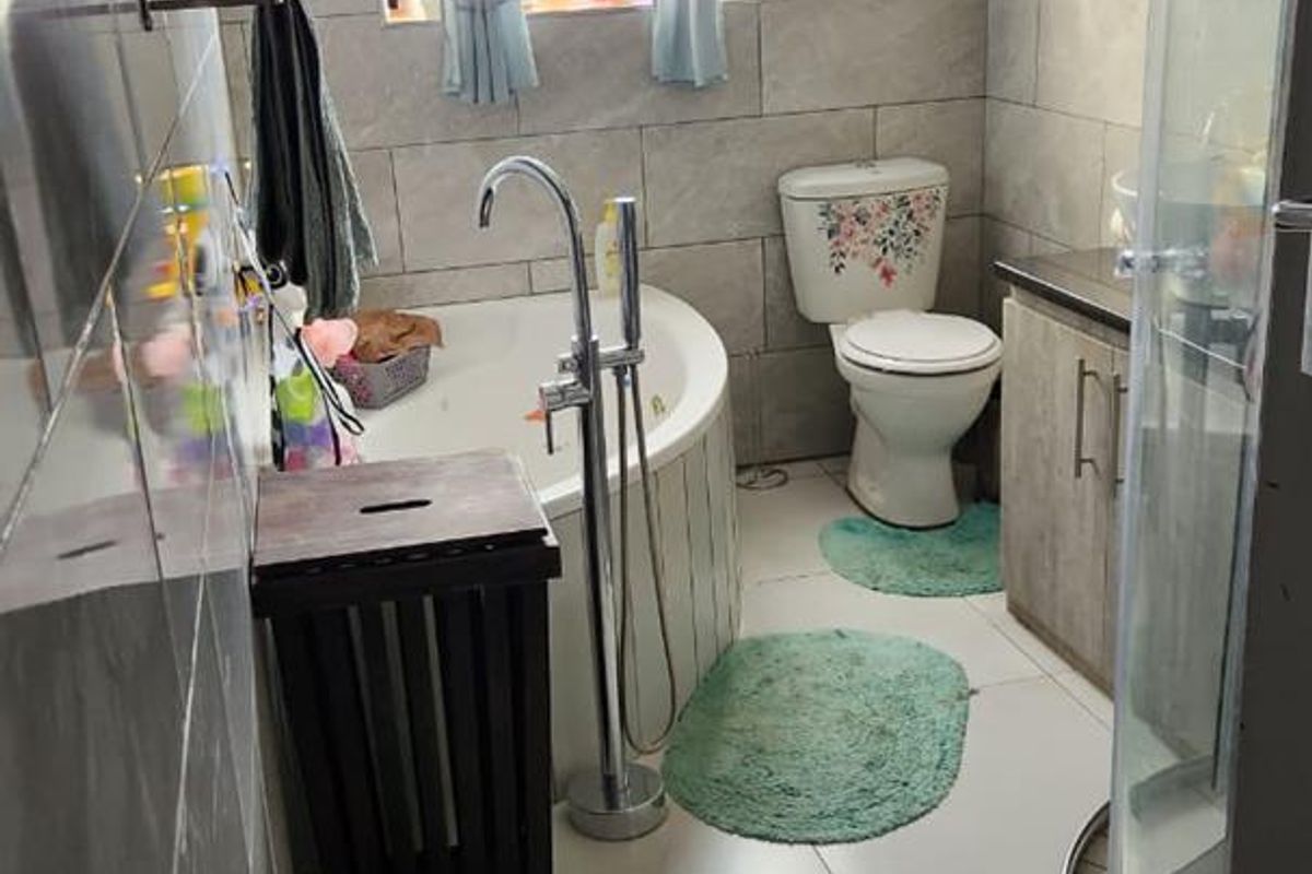 A functional bathroom featuring a corner bathtub, separate glass shower enclosure, vanity cabinet, and toilet with neutral wall and floor tiling.
