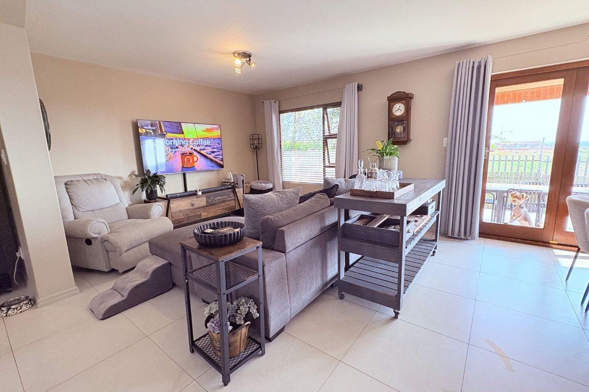 A bright and spacious living room featuring neutral tiled flooring, large windows, and a sliding glass door providing access to the outdoor area.