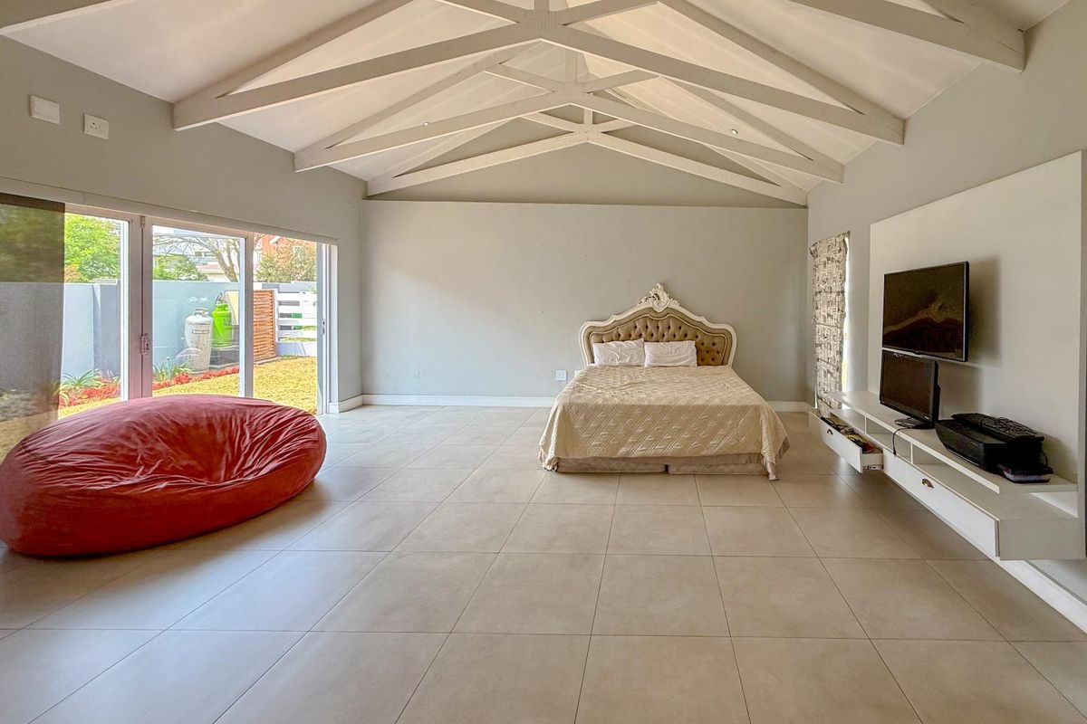 Spacious bedroom featuring a high vaulted ceiling with exposed timber trusses, large format floor tiles, and sliding glass doors opening to the garden.