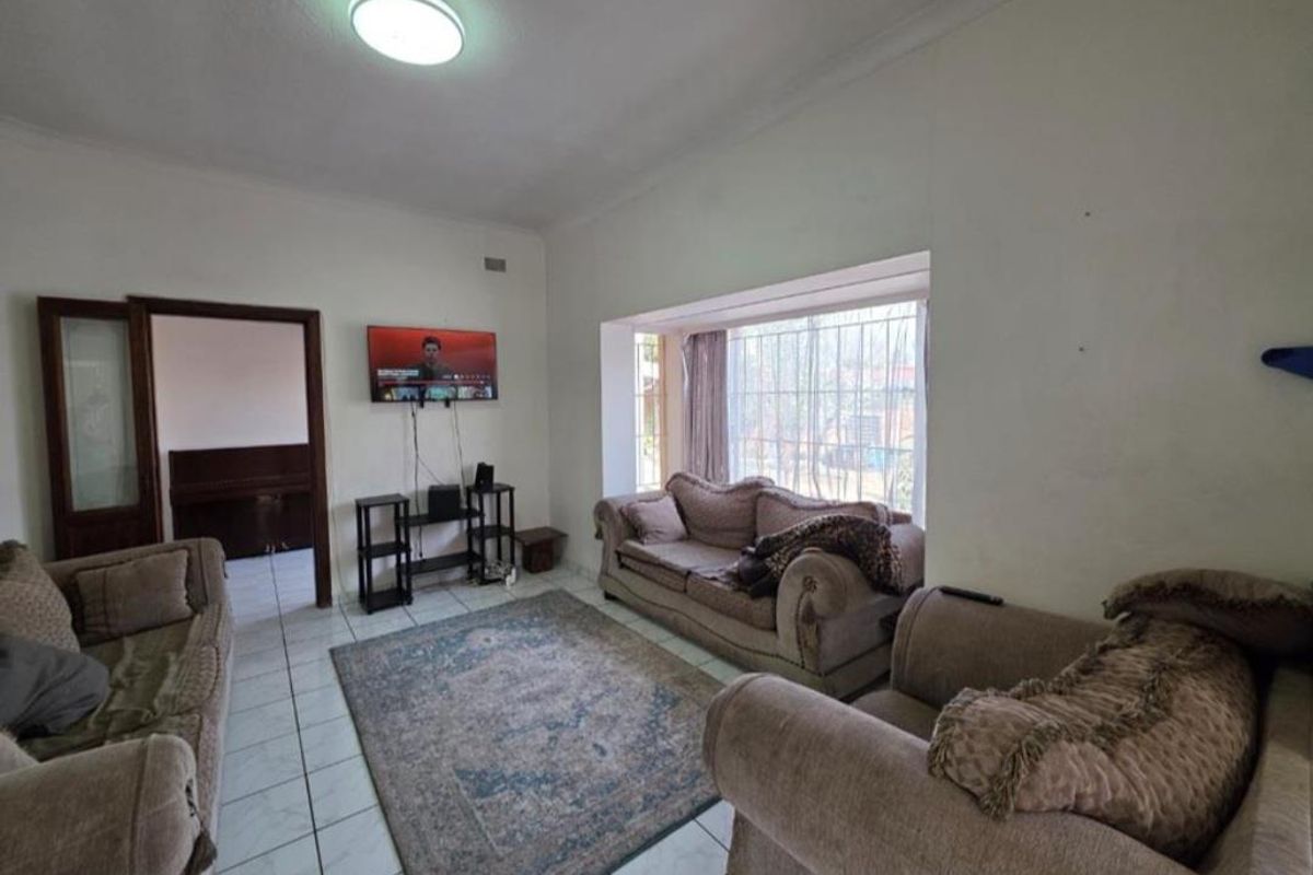A spacious living room featuring large bay windows, tiled flooring, and a ceiling-mounted light fixture, providing a comfortable and functional living space.