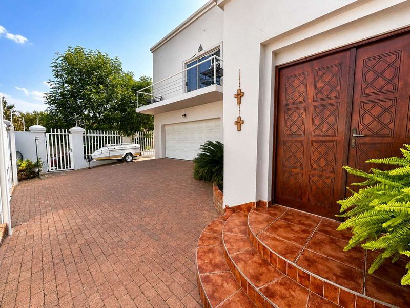 Front exterior view featuring a paved driveway, double wooden entrance doors with tiled steps, a garage, and an upper-level balcony with metal railings.