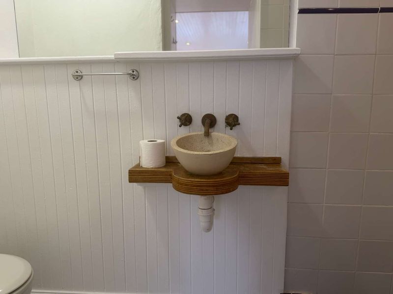 A compact bathroom featuring a unique wall-mounted stone basin, exposed plumbing, and classic white beadboard wall paneling.