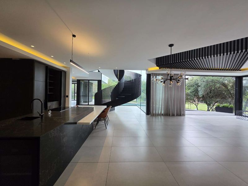 Modern open-plan living area featuring a sleek kitchen island, striking spiral staircase, and expansive sliding glass doors opening to the garden.