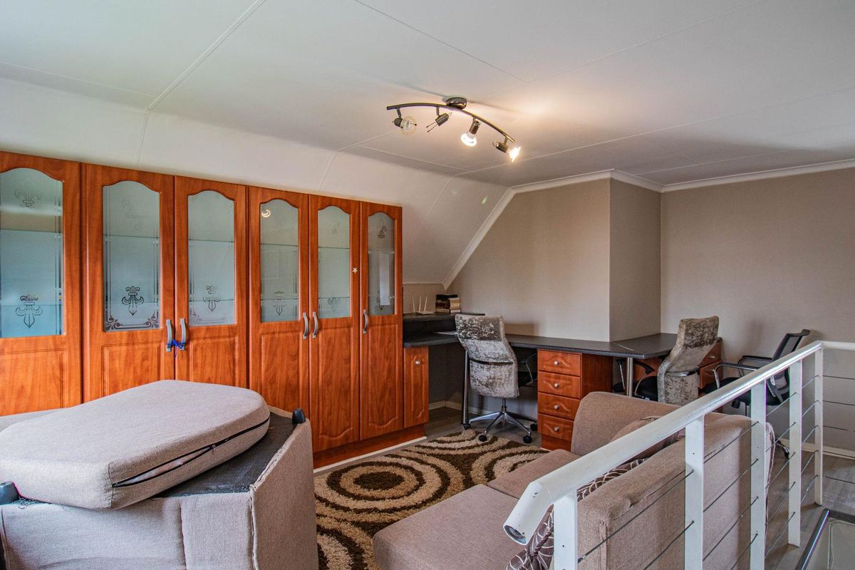A versatile loft space featuring extensive built-in wooden cabinetry, integrated desk workspace, and a modern metal balustrade overlooking the lower level.