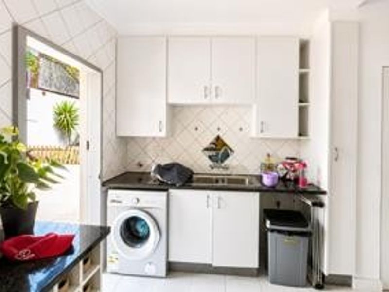 A functional laundry area featuring white built-in cabinetry, a dark countertop with an integrated sink, and tiled backsplash.