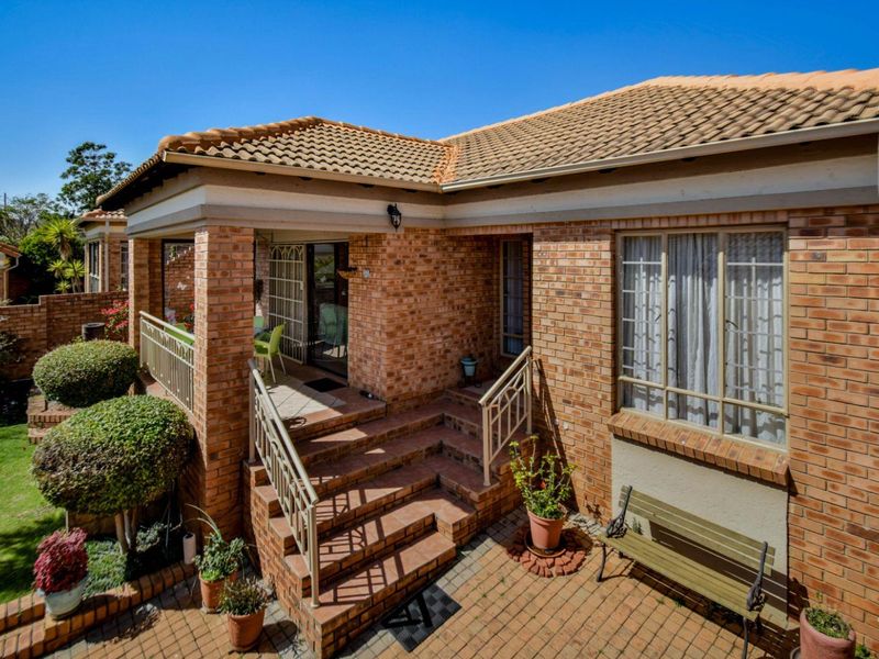 A well-maintained rear exterior view of a brick townhouse featuring a covered patio, paved courtyard area, and established garden surroundings.