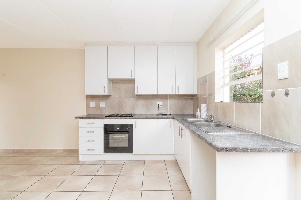 A clean, functional kitchen featuring white cabinetry, laminate countertops, a built-in oven with gas hob, and neutral tiled flooring and splashbacks.