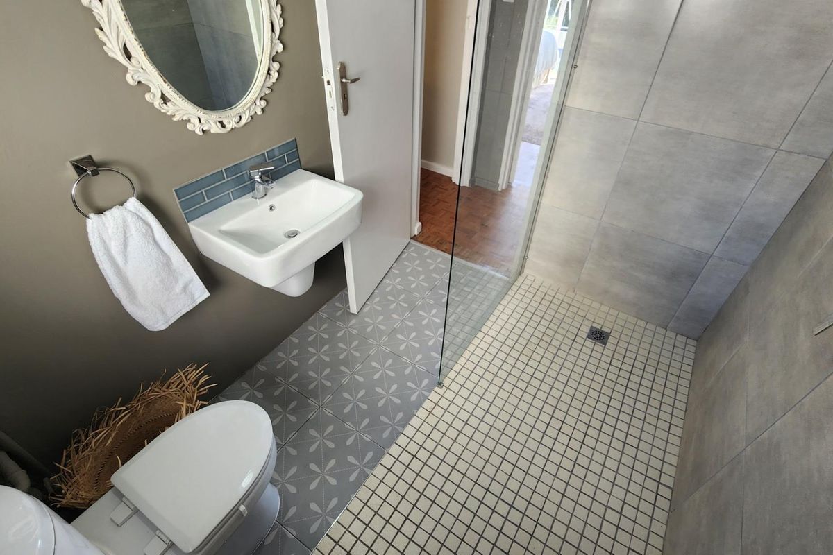 Modern bathroom featuring a walk-in shower with glass screen, wall-mounted basin, and contemporary patterned floor tiles.